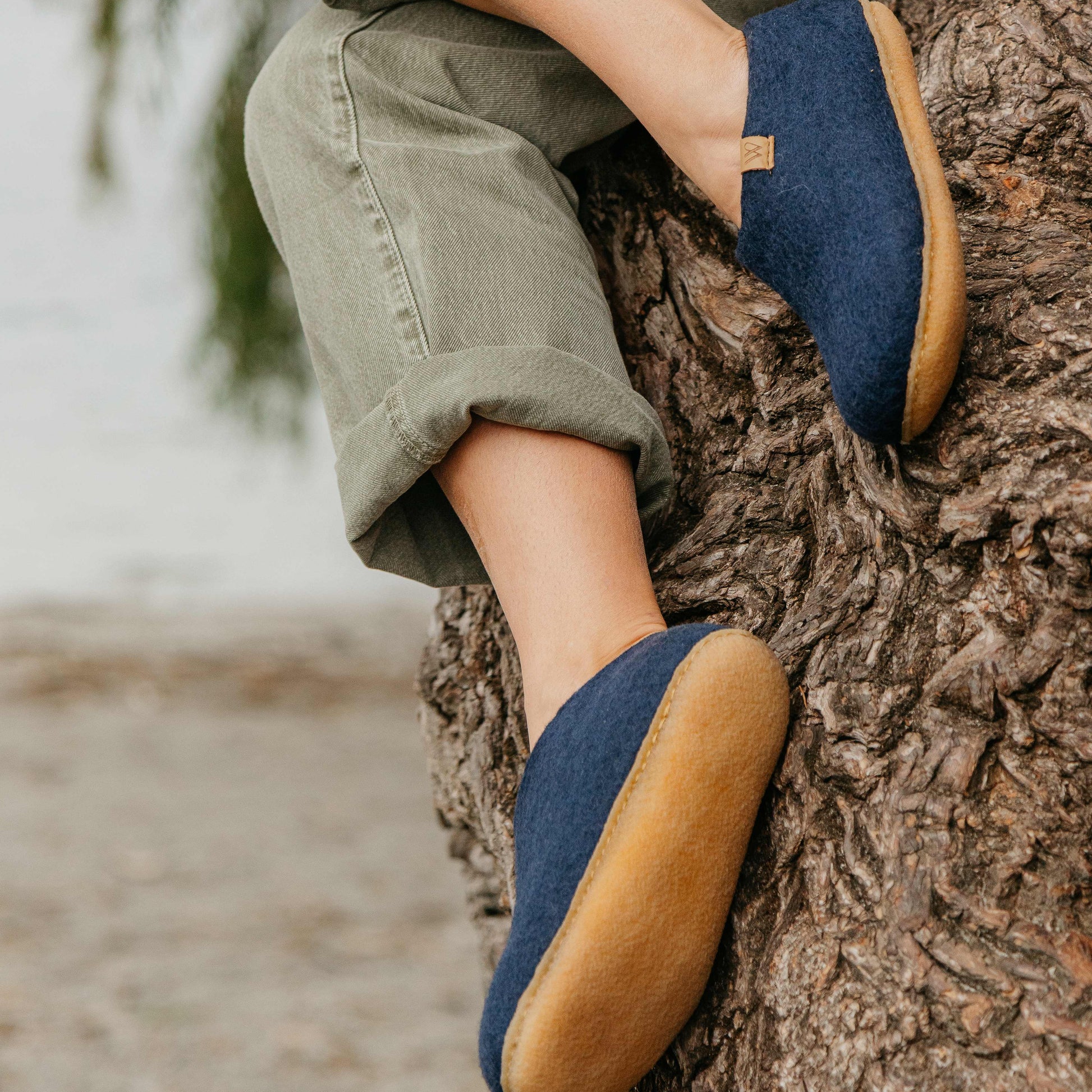 Person wearing blue shoes with brown soles sitting on a tree trunk.