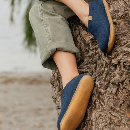 Person wearing blue shoes with brown soles sitting on a tree trunk.